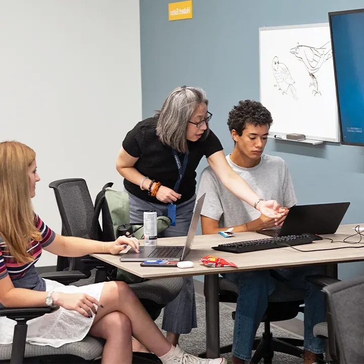 Professor pointing at laptop screen with student looking on.